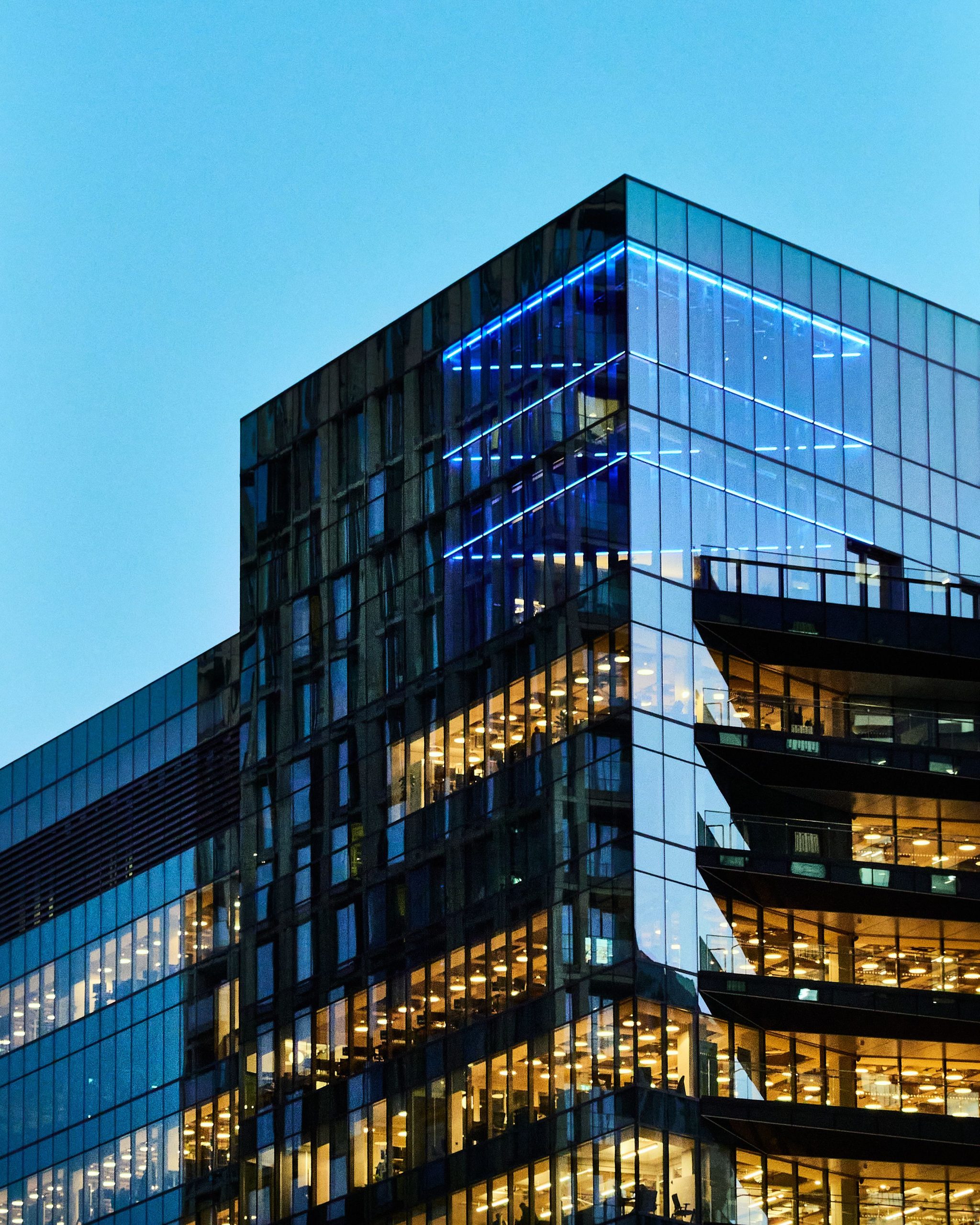 A sleek glass office building with illuminated interior visible against a twilight sky.